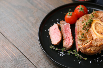 Pieces of delicious beef meat, spices and tomatoes on wooden table, closeup. Space for text