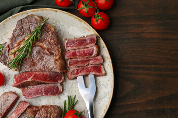 Pieces of delicious beef meat, spices and tomatoes on wooden table, flat lay. Space for text