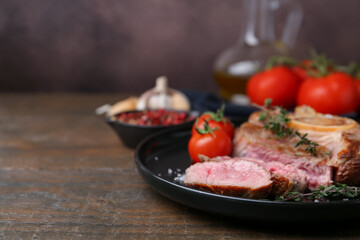 Pieces of delicious beef meat, spices and tomatoes on wooden table, closeup. Space for text