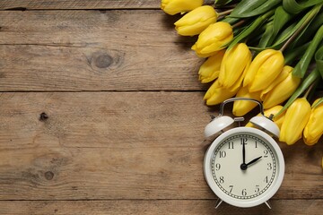 Spring time. Alarm clock and beautiful tulips on wooden table, flat lay. Space for text