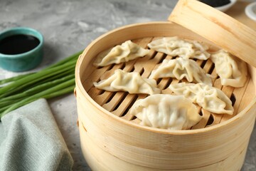 Tasty boiled gyoza (dumplings) in bamboo steamer on light grey table, closeup