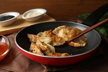 Taking tasty fried gyoza (dumpling) with chopsticks on table, closeup
