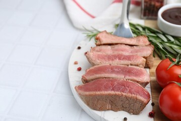 Delicious sliced beef tenderloin with different degrees of doneness, tomatoes and spices on light tiled table, closeup. Space for text