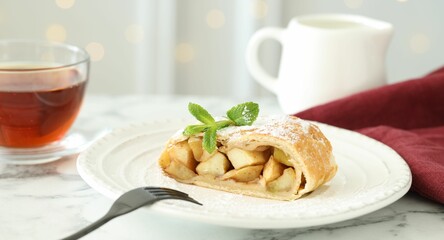 Piece of tasty apple strudel served with tea on white marble table, closeup