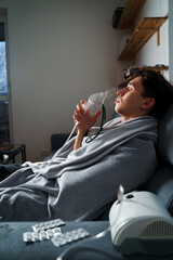 Man inhaling through oxygen mask for cough treatment. Using compressor nebulizer for disease...