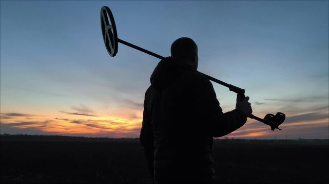 silhouette of a man with a metal detector against the sunset. Silhouette of a man along the field with a metal detector against the backdrop of a beautiful sunset.