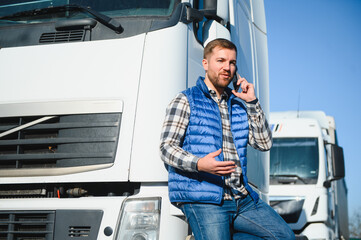 Professional driver using mobile phone while standing in front of his truck. Copy space