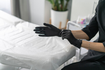 A cosmetologist is getting ready to perform a skincare treatment by putting on black gloves. The...