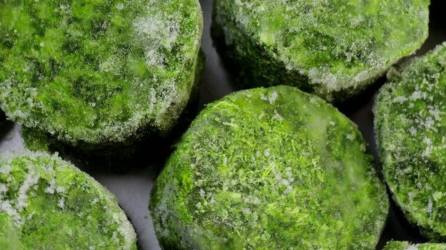 Frozen spinach blocks rotating in a circle. Close-up of icy green vegetable cubes, concept of frozen food, healthy eating, and meal preparation.