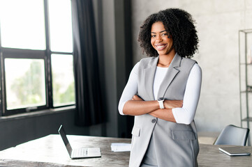 An African-American businesswoman stands by a window in a well-lit office, her smartwatch hinting...