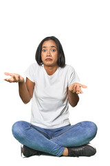 Latina sitting on floor in studio doubting and shrugging shoulders in questioning gesture.