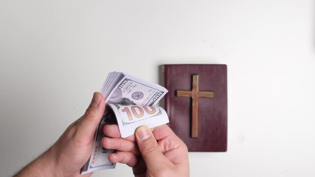 Counting one hundred dollar bills with bible and cross in background 