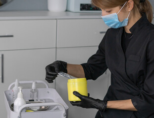 A cosmetologist with gloves and a mask carefully applies painkiller cream from a yellow container while preparing for a skincare treatment in a calm setting