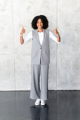 A cheerful African-American businesswoman stands with thumbs up, her vibrant smile and positive...