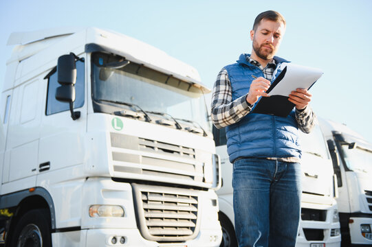 Truck driver checking shipment list while standing on parking lot of distribution warehouse