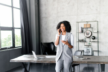 Cheerful African-American businesswoman enjoys a light-hearted phone conversation, her casual...