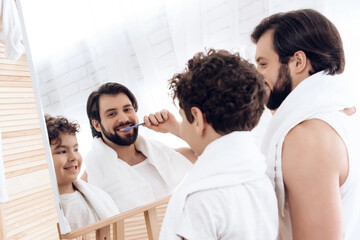 Naklejka premium Happy father and son brush teeth with toothbrush, looking in mirror.