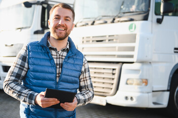 Happy confident male driver standing in front on his truck, using his tablet