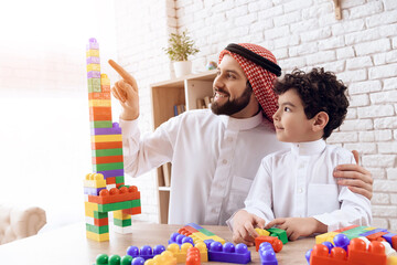 Arab man with little boy builds tower of colored plastic blocks.