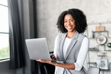 A radiant African-American businesswoman holding laptop, embodying the spirit of modern...