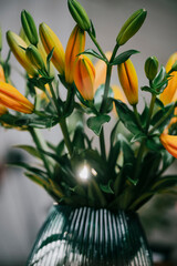 A vase of yellow and green flowers sits on a table. The flowers are in full bloom and are arranged in a way that makes them look like they are reaching up towards the light