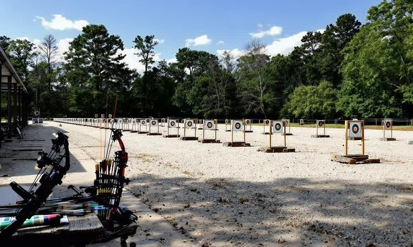Outdoor Archery Range On Sunny Day Rows Of Targets On Gravel Grounded Area With Trees And Equipment Visible In Foreground Under Partly Cloudy Sky. Ideal For Sports, Recreation, Or Competition