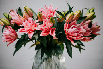 A vase full of pink flowers sits on a table. The flowers are arranged in a way that they are all facing the same direction, creating a sense of harmony and balance. The vase itself is clear
