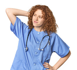 Young Caucasian redhead woman as nurse touching back of head, thinking and making a choice.