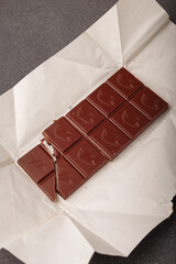 whole but broken bar of dark chocolate with grinded cocoa beans on kraft paper package, top view.