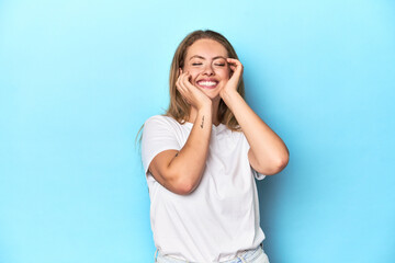 Blonde young woman in white t-shirt on blue background whining and crying disconsolately.