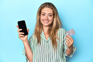Young blonde woman holding a credit card and a mobile phone in a studio