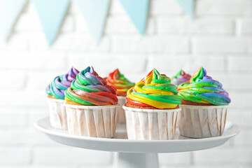 Delicious cupcakes with colorful cream on stand near white brick wall, closeup