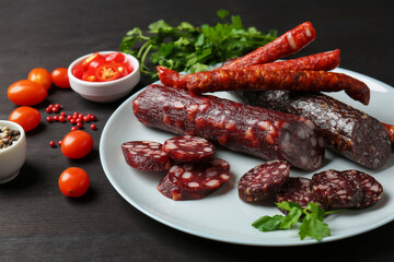 Different smoked sausages, cherry tomatoes and spices on dark wooden table, closeup