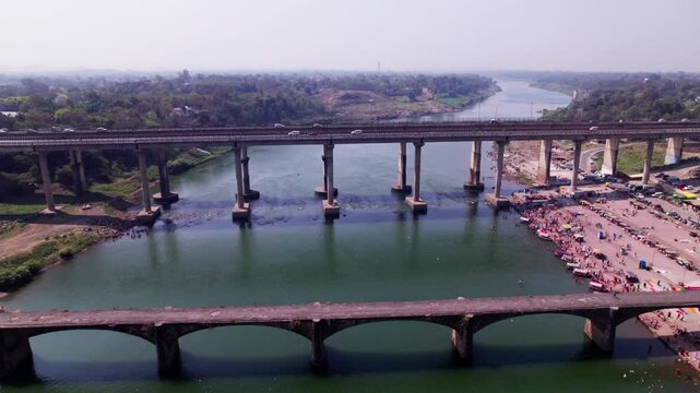 Tilwara Narmada River Bridge with flying birds and boats at narmada ghat, tilwara, jabalpur, madhya pradesh, india. day time, push in, tilt down, drone shot, 4k.