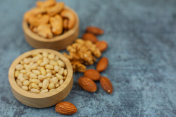 Close-up of wooden bowls with pine nuts, bowls of cashews out of focus, which stand on the side surrounded by walnuts and almonds on a gray background with space for text. The concept of healthy