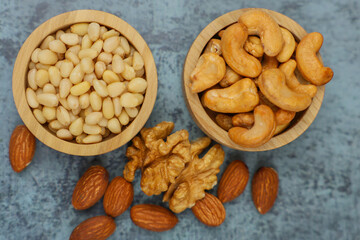 Close-up view from above of wooden bowls with pine nuts and cashews, which stand on the side surrounded by walnuts and almonds on a gray background. The concept of healthy snacks, healthy and