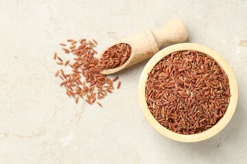 Brown rice in bowl and scoop on light grey table, flat lay. Space for text