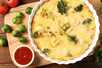 Delicious vegetable casserole, sauce and ingredients on wooden table, flat lay