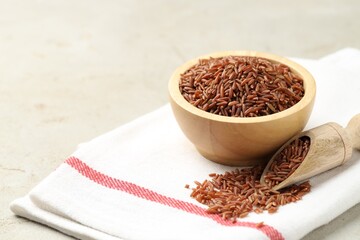 Brown rice in bowl and scoop on light grey table, closeup. Space for text