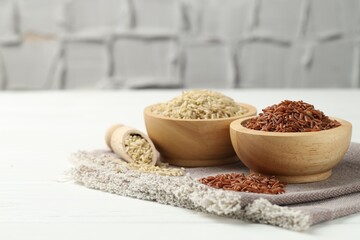 Different types of brown rice in bowls and scoop on white wooden table, closeup. Space for text