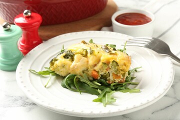 Tasty vegetable casserole, arugula and fork on white marble table, closeup