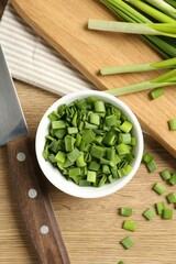 Cut fresh green onions in bowl and knife on wooden table, flat lay