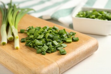 Whole and cut fresh green onions on white table, closeup