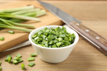 Cut fresh green onions in bowl and knife on wooden table, closeup