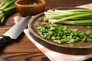 Fresh green onions and knife on wooden table, closeup