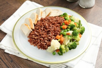 Delicious brown rice with chicken and vegetables served on wooden table, closeup