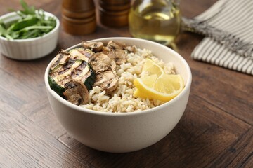 Delicious brown rice with mushrooms, zucchini and lemon slices served on wooden table, closeup