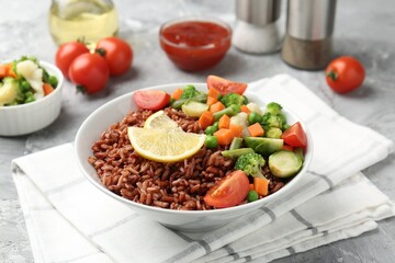 Delicious brown rice with vegetables and lemon slices served on grey textured table, closeup