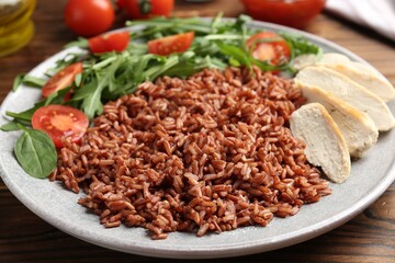 Delicious brown rice with chicken and salad served on wooden table, closeup