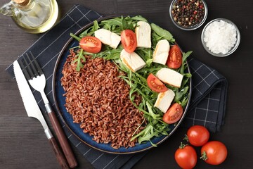 Delicious brown rice with chicken, arugula and tomatoes served on black wooden table, flat lay
